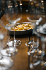 Pasta dish framed by blurred wine glasses on a wooden table