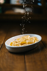 Grated cheese falling onto creamy pasta in a white dish