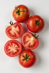 A top view of fresh red tomatoes, some whole and some cut in half, on a plain white background