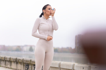 Woman using asthma inhaler for breath relief outdoors
