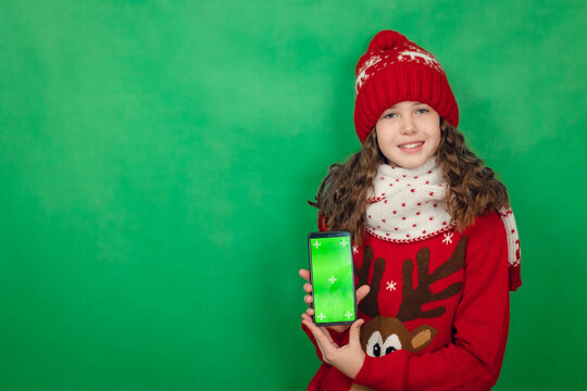 Teenage girl in santa hat on red background holding laptop with green screen, copy space, chroma key - Powered by Adobe