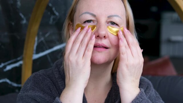Adorable curly woman glancing straight on camera. Happy woman smiling and using gold eye patches with collagen, peptide, ceramide and hyaluronic acid, derma oil. Dermatology, healthy skin concept.