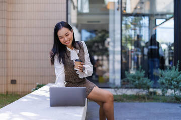 Asian businesswoman remote working with laptop and coffee outdoors