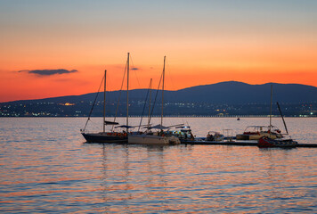 Sailing yachts on the water at sunset with an orange sky and mountain silhouettes