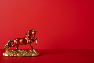 Side view of a gleaming gold horse statue on a red surface, symbolizing fortune and speed. A festive Chinese New Year mood with luck, prosperity and greeting