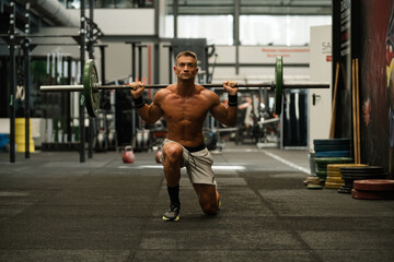 Shirtless man performing barbell lunge in gym