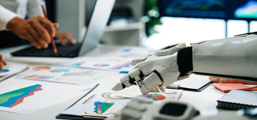 A futuristic office scene showcasing a robot and a human working together on business charts, highlighting the integration of technology in modern analytics.Noogenesis