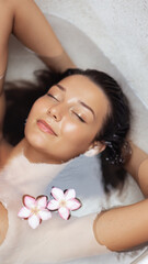 Asian Woman Relaxing in Bath With Plumeria Flowers and Glowing Skin