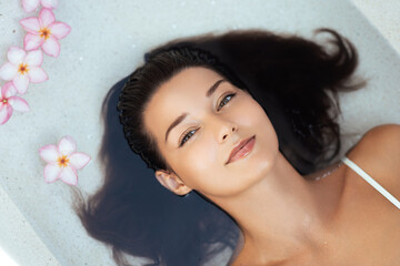 Young Woman Resting In Luxury Spa Bath With Frangipani Flowers Concept