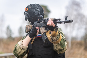 Obraz premium Russian special forces soldier holds a Kalashnikov assault rifle in his hands and stands in sight. Russian assault military forces soldiers at combat action. military exercises in the Russia army.