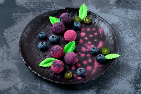 Chocolate truffles covered with freeze-dried berry powder on a black plate. Pink and purple candies. Top view