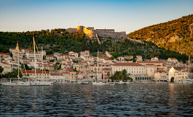 Scenic view of a coastal town at sunset with boats in the harbor and hills in the background
