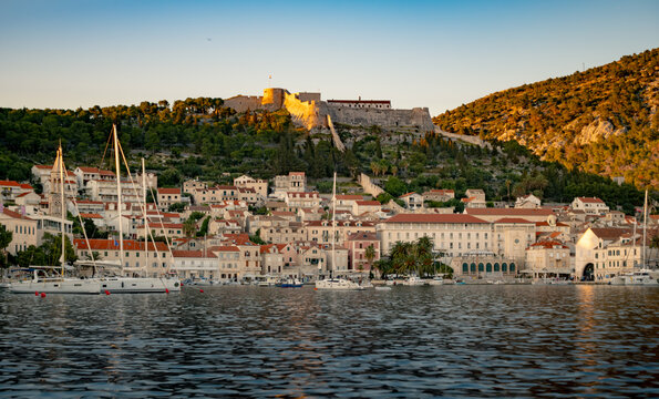 Scenic view of a coastal town at sunset with boats in the harbor and hills in the background