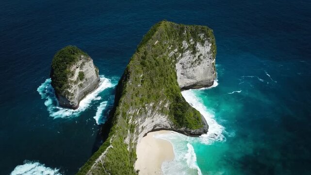 Smooth drone orbit shot rotating around the iconic Kelingking "T-Rex Head" cliff on Nusa Penida. Showcases the steep green cliff and the secluded turquoise beach below.