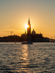 Obraz premium Vertical composition of Venice sunset with blazing sun aligned over San Giorgio Maggiore bell tower and golden light path stretching across dark rippling lagoon.