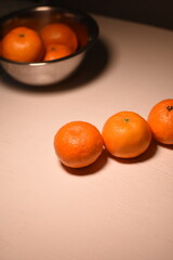 Three tangerines in a row, slightly from above at an angle, with a blurred metal bowl of tangerines in the background.