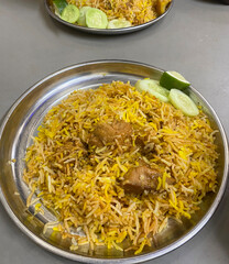 A closeup view of a delicious plate of yellow chicken biryani served with cucumber slices