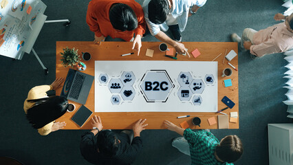 A dynamic team collaborating on B2C strategies displayed on a wooden table, with digital devices and notes, fostering innovation and effective communication in an office environment. Trope