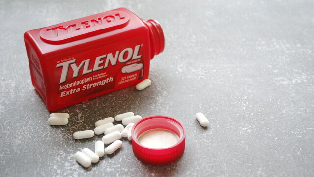 bangkok, thailand - 09 28 2025 : Tylenol Extra Strength acetaminophen pills spilled from a red bottle on a grey surface, suggesting pain relief and medication.