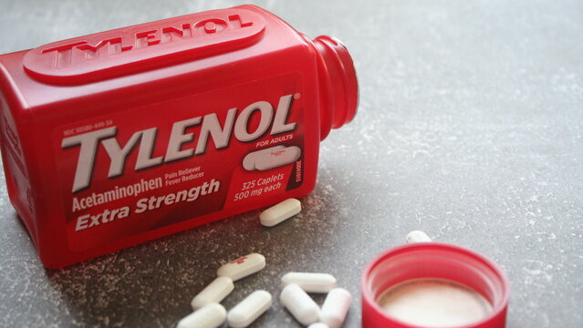 bangkok, thailand - 09 28 2025 : Tylenol Extra Strength acetaminophen pills spilled from a red bottle on a grey surface, suggesting pain relief and medication.