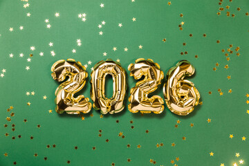 New year 2026 balloon celebration card. Gold foil helium balloon number 2026, party decoration, gold confetti stars on green background. Copy space, flat lay, merry christmas, happy holidays concept.