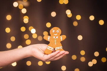 gingerbread man in female hands on christmas background among new year lights