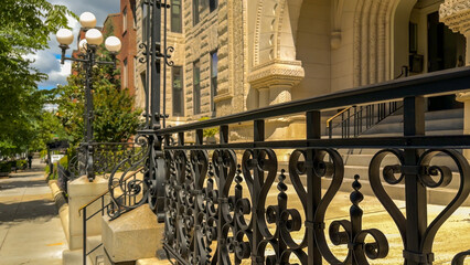 Decorative wrought iron railing and vintage lamp posts line the entrance of a historic stone building