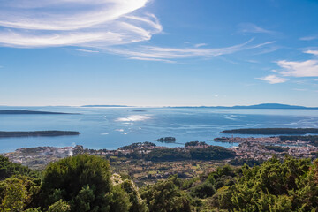 A panoramic view reveals the Rab island coastline and vast Adriatic Sea from Mount Kamenjak. Wispy clouds float in blue sky over the historic town, highlighting beauty of the Kvarner region, Croatia