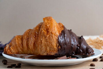 Chocolate-dipped croissant with coffee beans on a plate