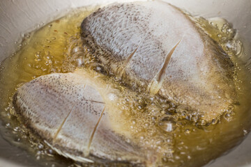 Close-up of Thai-style snakeskin gourami being fried in a pan with boiling oil, showing crispy golden texture.