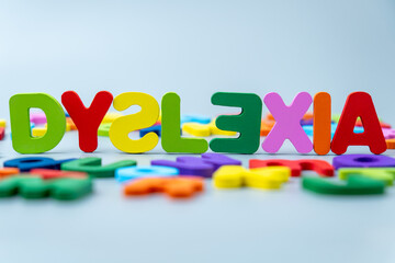 The word DYSLEXIA is spelled out in colorful wooden letters scattered on a gray background. Learning difficulties, neurodiversity, educational challenges, reading struggles, and cognitive support.