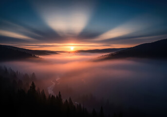 Sunrise over foggy mountain valley with river and glowing clouds at dawn.