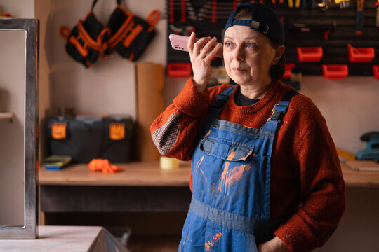 Mechanic woman in blue coveralls listening voice message in workshop
