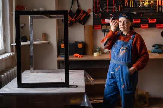 Mechanic woman in blue coveralls listening voice message in workshop