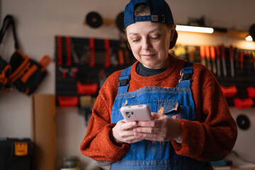 Smiling mechanic woman browsing on her mobile phone in a restoring repair shop