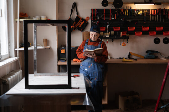 handyman mechanic in workshop writing notes in notepad while repair furniture. Small business
