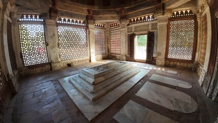 Fototapeta premium Interior View of the Tomb of Imam Zamin, Highlighting the Central Marble Cenotaph and the Intricate Geometric (Lattice) Windows that Filter Sunlight onto the Floor and Walls of the Modest Chamber