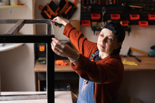 Handyman measuring metal legs in workshop with tape measure during furniture assembly. Concept of furniture making