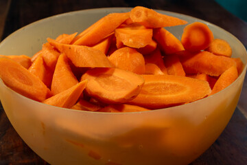 Freshly sliced carrots in a translucent bowl rest on a dark wooden surface