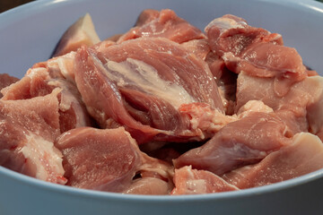 Freshly cut raw meat with visible muscle fibers and fat rests in a light-colored bowl, ready for preparation.