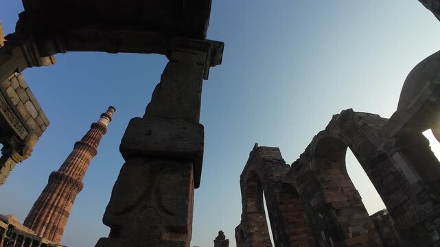 Low-Angle Perspective of the Historic Qutub Minar (Minaret) Tower, Framed by the Ancient Stone Pillars and Arches of the Quwwat-ul-Islam Mosque Ruins in the UNESCO World Heritage Site in Delhi, India