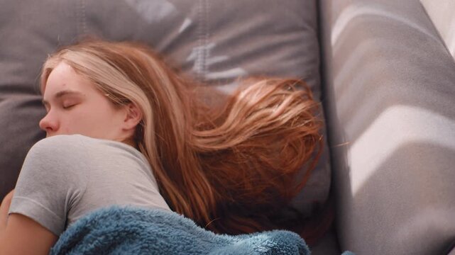 Top down view of morning beauty sleeping peacefully with long hair spread across couch while holding fluffy blanket under soft daylight casting gentle shadows across calm intimate interior scene