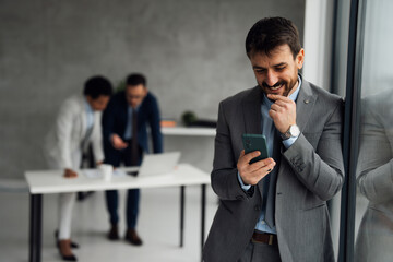 Businessman using his mobile phone in an office, with colleagues working in the background.