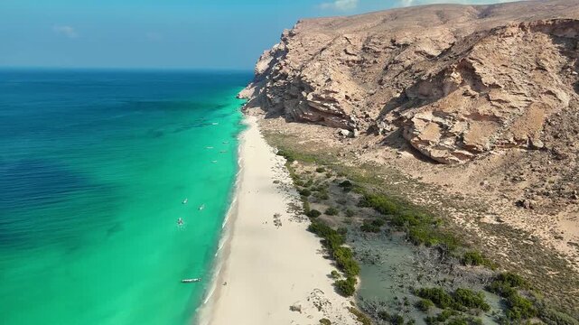 Drone view of stunning coastal landscape with clear turquoise water, soft white sand, and towering rocky cliffs, where small boats create a serene and picturesque seaside atmosphere. Socotra island