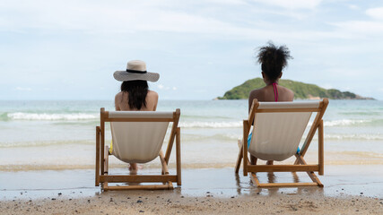 Two women relaxing on beach chairs facing the calm ocean, enjoying a peaceful tropical atmosphere. 