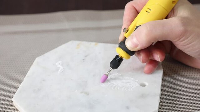 Woman using a hand engraver with a ceramic attachment to engrave a design on marble, close-up