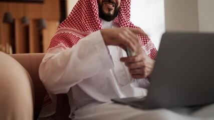 Glad Arab man counting money by laptop, celebrating successful crypto gains - Powered by Adobe