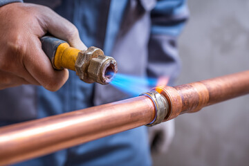 A plumber uses a blowtorch to solder a copper pipe connection, creating a permanent, leak-proof seal