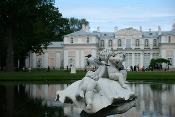 A seagull on the white marble statue "Triton" against the backdrop of the palace in Oranienbaum Park. Sculptor Joseph von Kopf, 1861