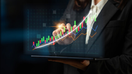 A businesswoman holds a tablet displaying colorful graphs and charts, symbolizing market trends and financial growth in a modern office environment. Impute
